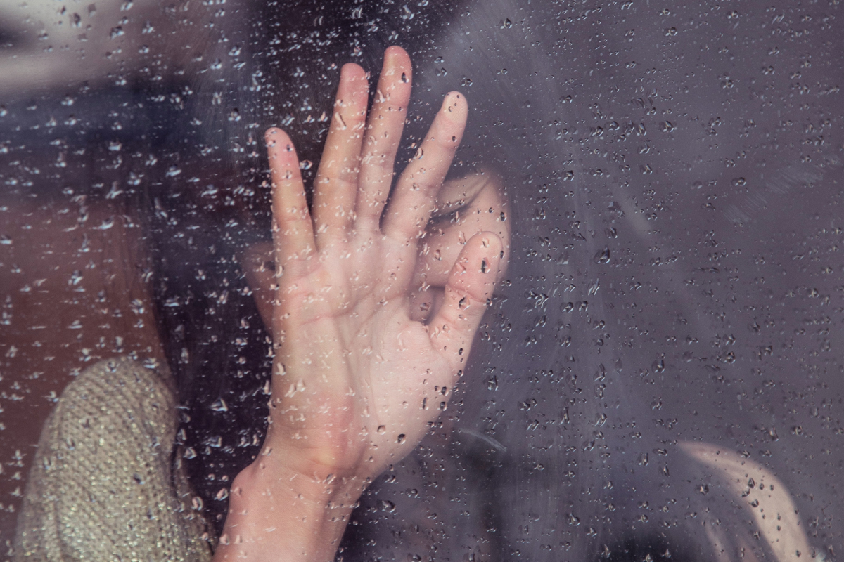 Chica apoyada en una ventana mientras afuera llueve